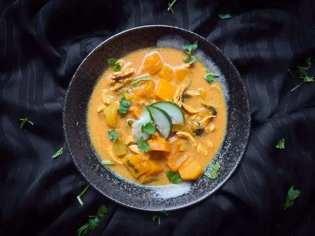 The coconut broth, shredded chicken, and butternut squash are presented in a blue bowl.