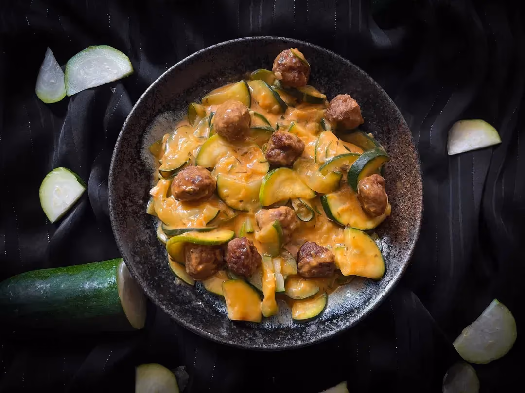 In a small blue bowl are the beef meatballs, zucchini, and tomato cheese sauce.