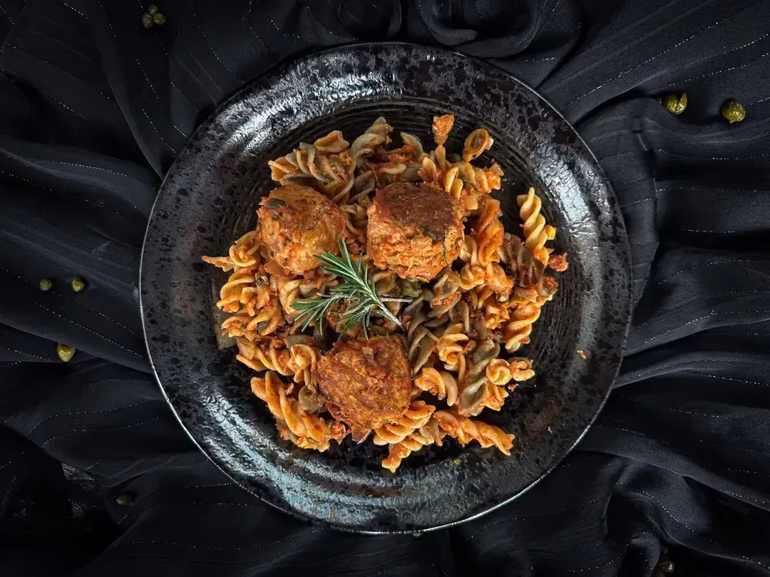 Un petit saladier de couleur bleu accueille trois grosses boulettes de thon à la sauce tomate et des pâtes de lentilles corail.
