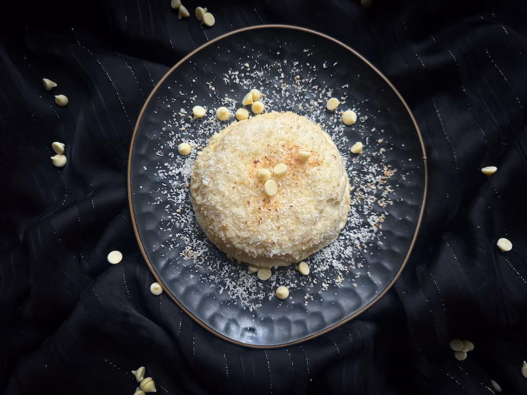 Le bowl cake est présenté dans une assiette noire, il est décoré d'un glaçage au chocolat blanc/noix de coco râpé.