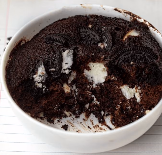 Dans un bol de couleur blanc se trouve la préparation du bowl cake Oreo. Trois biscuits Oreo se confondent avec le chocolat.