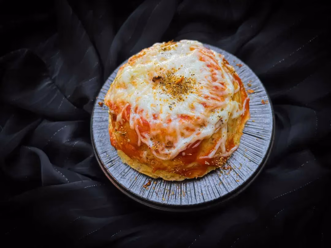 Dans un petit plat creux se trouve le Bowl cake façon pizza. Sur le dessus il y a du fromage râpé fondu.