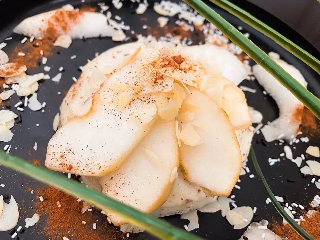 Déposées sur un plat de couleur noir, de grosses tranches de poire sont saupoudrées d'amandes effilées qui servent de topping.
