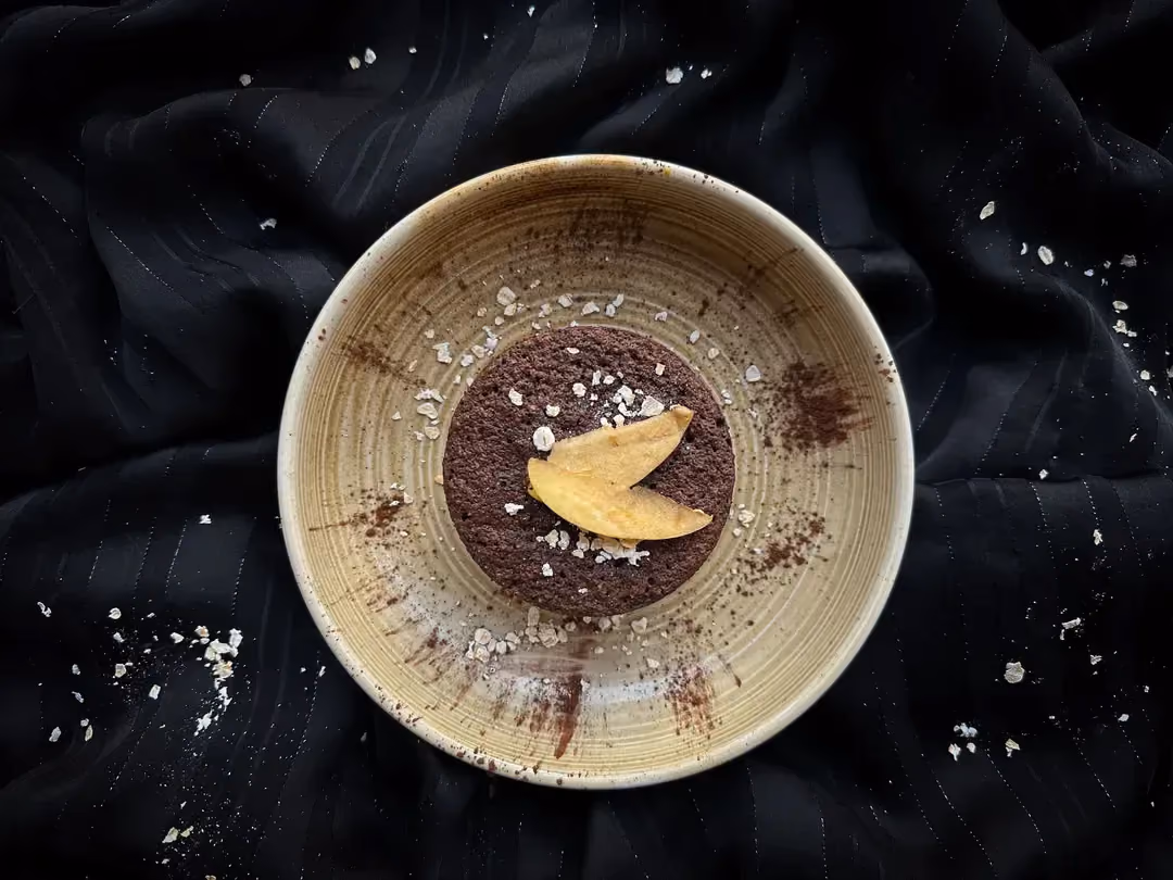 Sur une assiette bleue et blanche avec des motifs de feuillage, se trouve le bowl cake avec un saupoudrage de chocolat et des amandes concassées.
