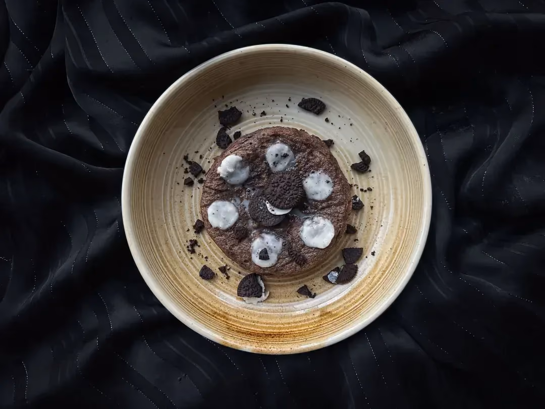 Sur un plat de couleur noir se trouve le bowl cake aux biscuits Oréo. Le topping est composé de deux biscuits Oréo.