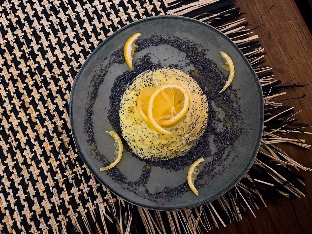 Dans un petit saladier se trouve le bowl cake protéiné aux graines de pavot. Une tranche de citron jaune sert de topping.