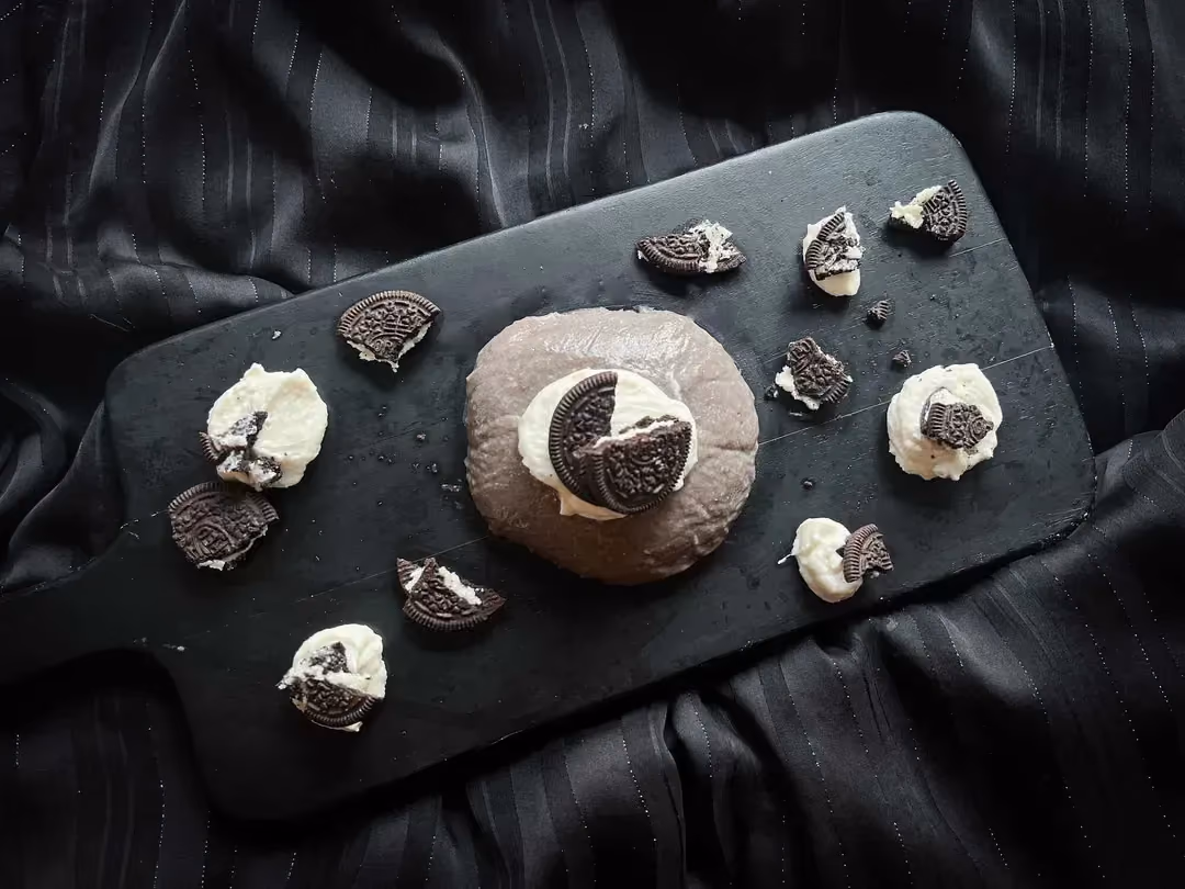 Le bowl flan Oréo est présenté sur une planche à découpé de couleur noire. Des petites morceaux de biscuits Oréo se trouvent à côté.