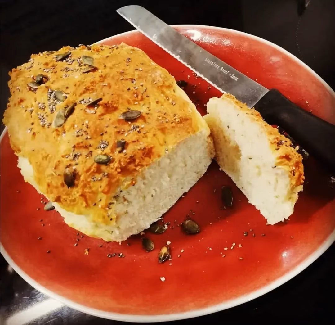 Sur une assiette de couleur rouge se trouve la brioche. Une tranche a été coupée avec un couteau à pain qui se trouve à côté.