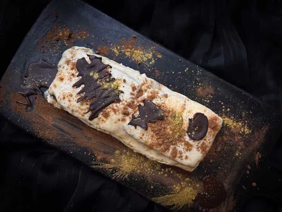 La magnifique bûche tiramisu au pain d'épices est présentée sur une planche à découper de couleur noire.