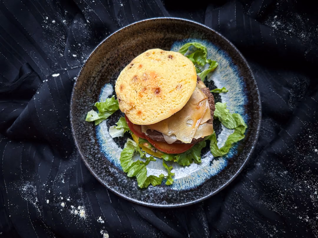 Présenté au centre d'une assiette de couleur noire et bleue, ce burger est un vrai régal pour les yeux. Il invite à un moment de pur plaisir.