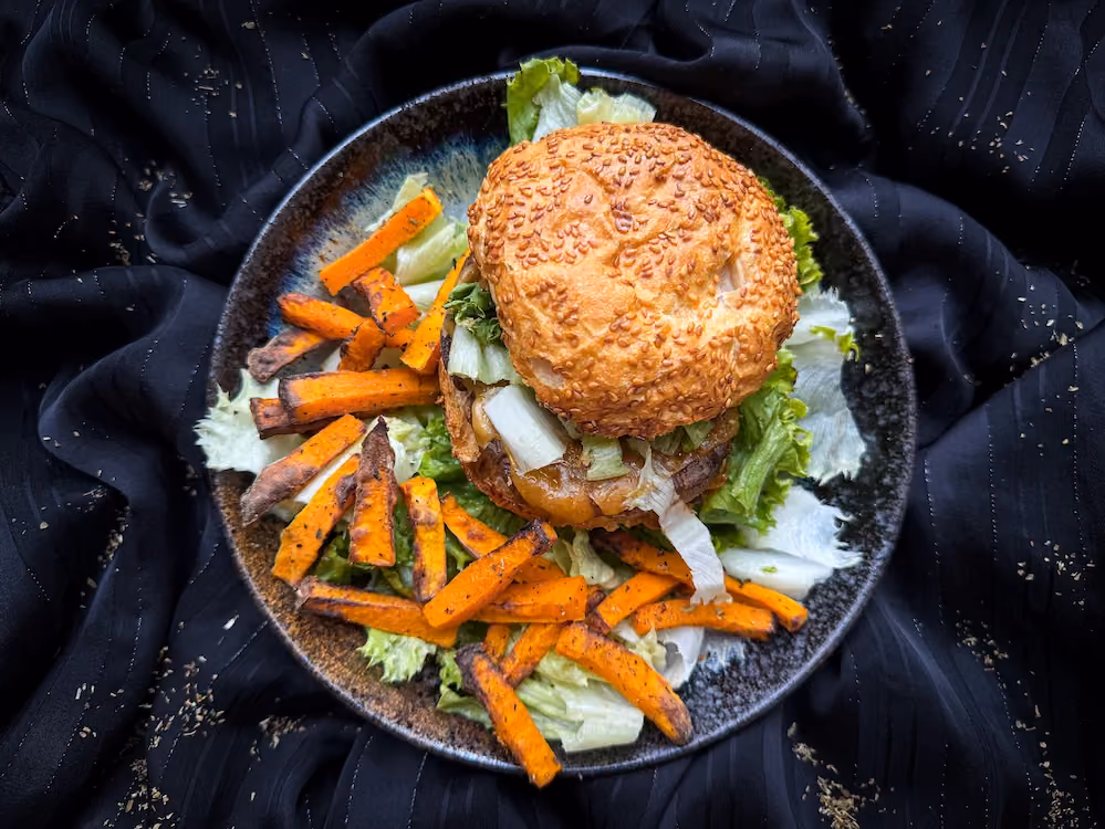 On a beautiful black earthenware plate, the ham burger is served with fries and a few lettuce leaves.