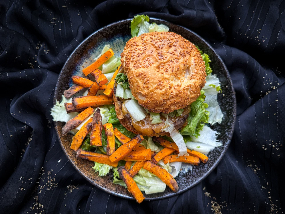 On a beautiful black earthenware plate, the ham burger is served with fries and a few lettuce leaves.