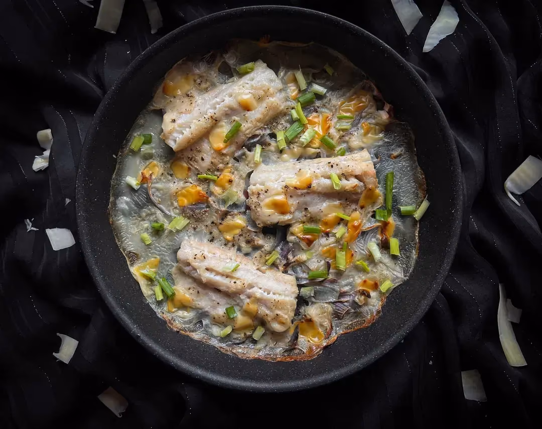 In a large mixing bowl, there are three large slices of cod with vanilla béchamel sauce.