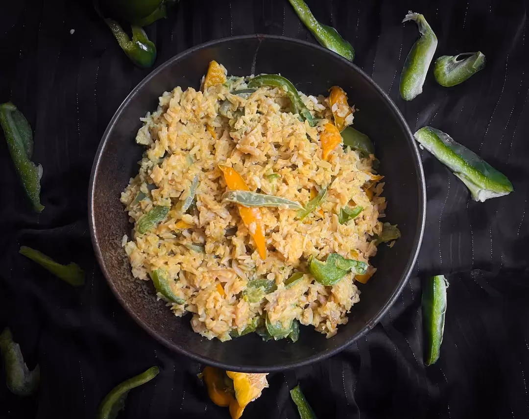 In a small bowl, there are bell peppers and rice with coconut curry sauce. A few small pieces of bell pepper are next to the dish.