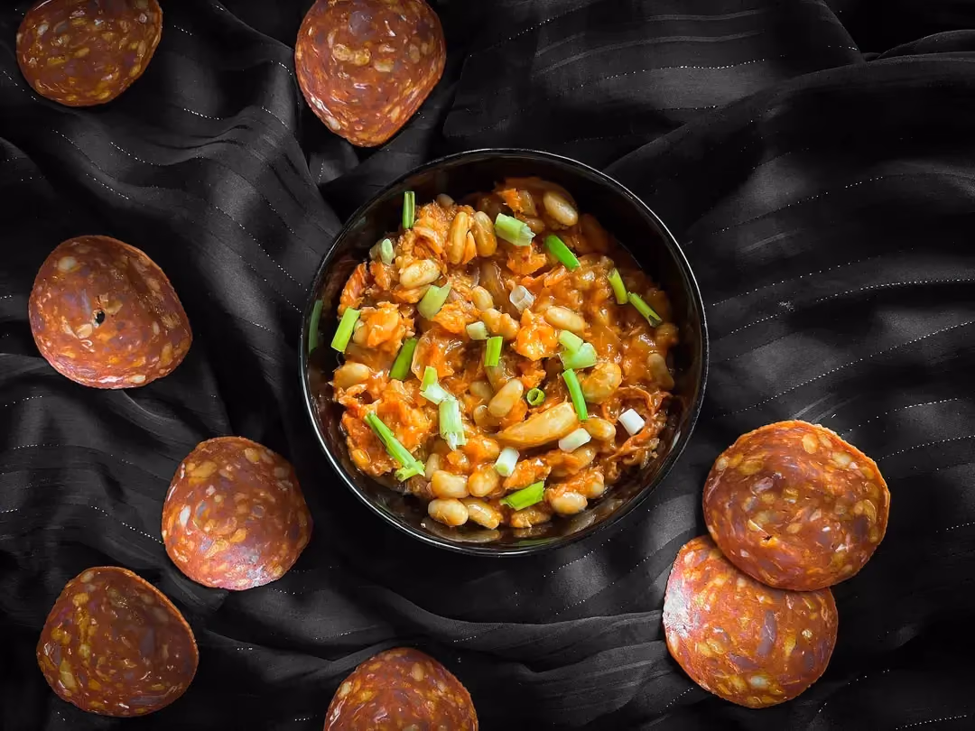 Cod with tomato sauce, white beans, and chorizo is served in a small bowl. Eight thin slices of chorizo accompany the dish.