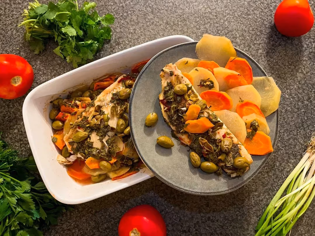 Sur une assiette, un filet de cabillaud accompagne des carottes et des pommes de terre coupées en fines rondelles et des olives vertes.