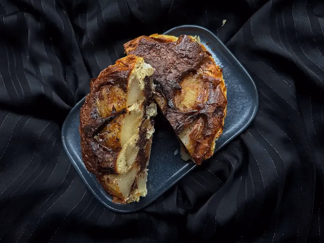 Sur une assiette de couleur blanche, le cake démoulé bien doré laisse apparaître quelques petits morceaux de poire et des pépites de chocolat.
