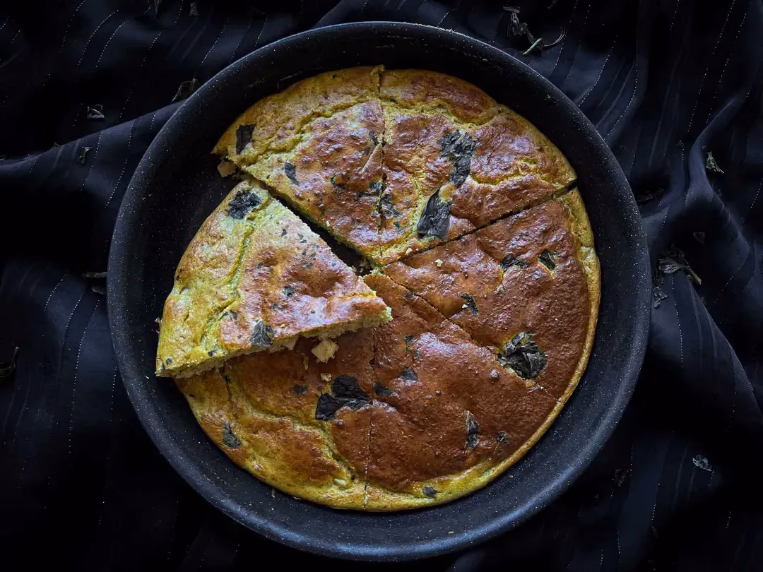 Le cake salé au pesto avec des dès de poulet est présenté dans un saladier profond. Il est déjà coupé en quatre parts inégales.