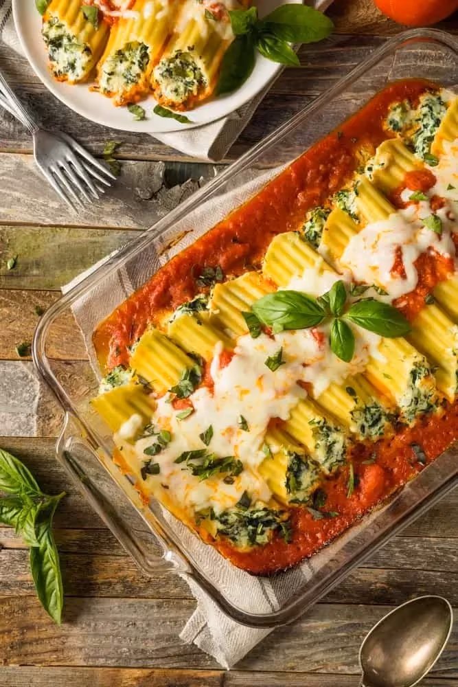 Dans un plat à gratin transparent, les cannelloni reposent sur un lit d'épinards, de tomates et de boeuf.