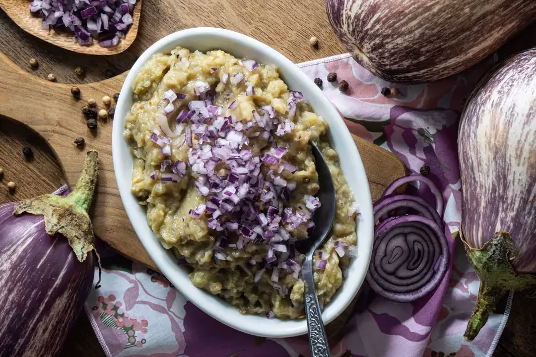 Dans un petit plat à gratin se trouve la purée d'aubergine. Trois grosses aubergines entières sont disposées autour.