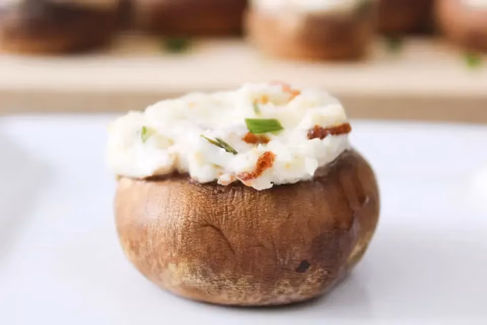 La tête d'un gros champignon de Paris est farcie avec du fromage frais et du bacon. Le fromage frais déborde largement du champignon.