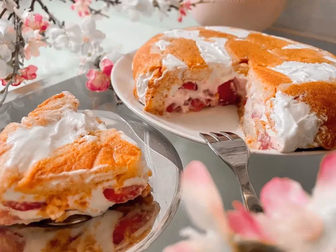 The strawberry charlotte is presented on a white plate in the background, and in the foreground there is a sliced piece.