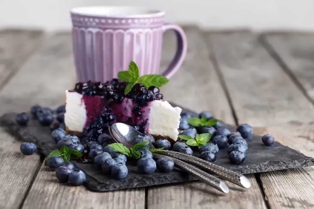Le cheesecake est présenté sur une ardoise et il est recouvert généreusement de myrtilles.