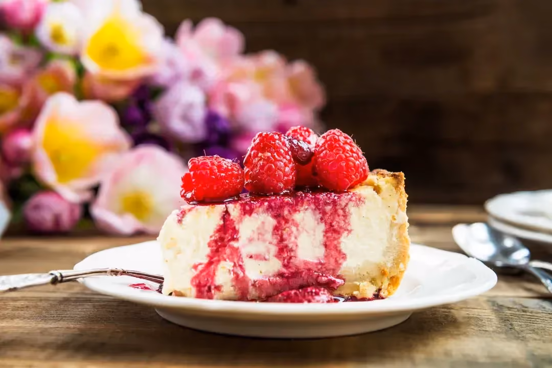 Posé sur une assiette de couleur blanche, un généreux morceau de cheesecake avec ses framboises.