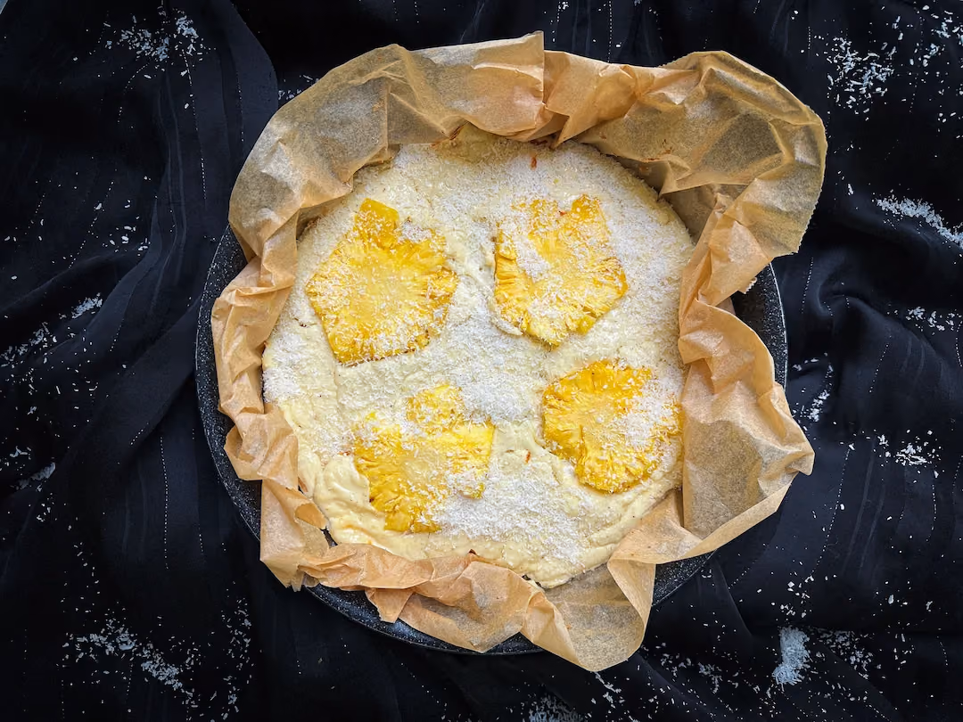 Présenté dans un moule de cuisson, le cheesecake est recouvert par des tranches d'ananas.