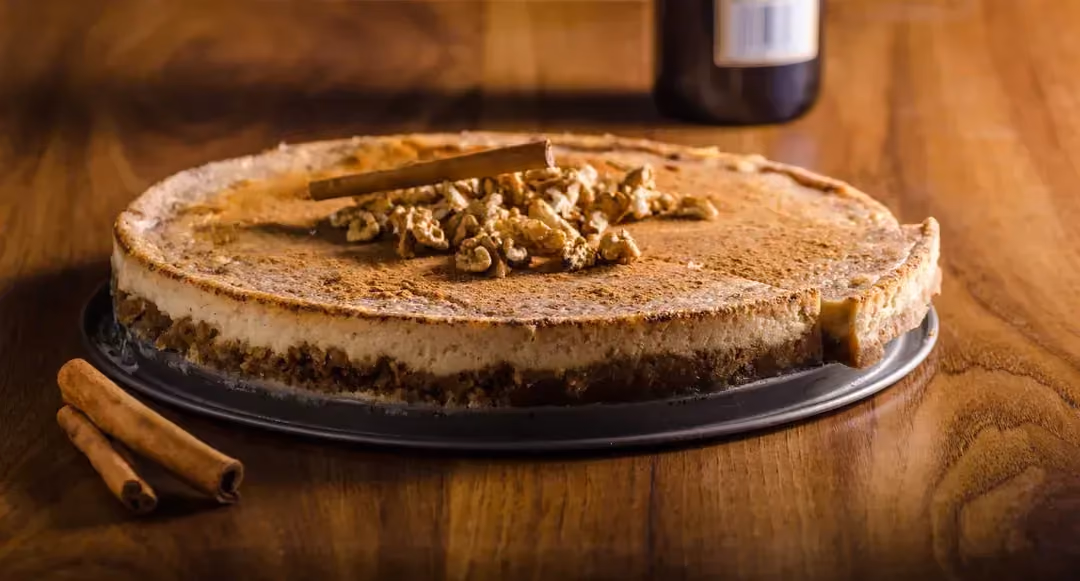 Présenté sur un plan de travail en bois foncé, le cheesecake est recouvert d'un topping au chocolat et aux noix.