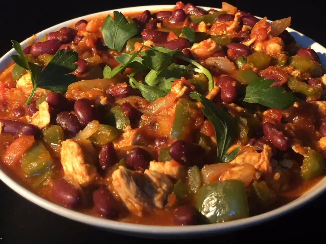 Dans un plat creux, se trouve le poulet coupé en généreux morceaux, les haricots rouges et le poivron baignant dans le chili et la sauce tomate.