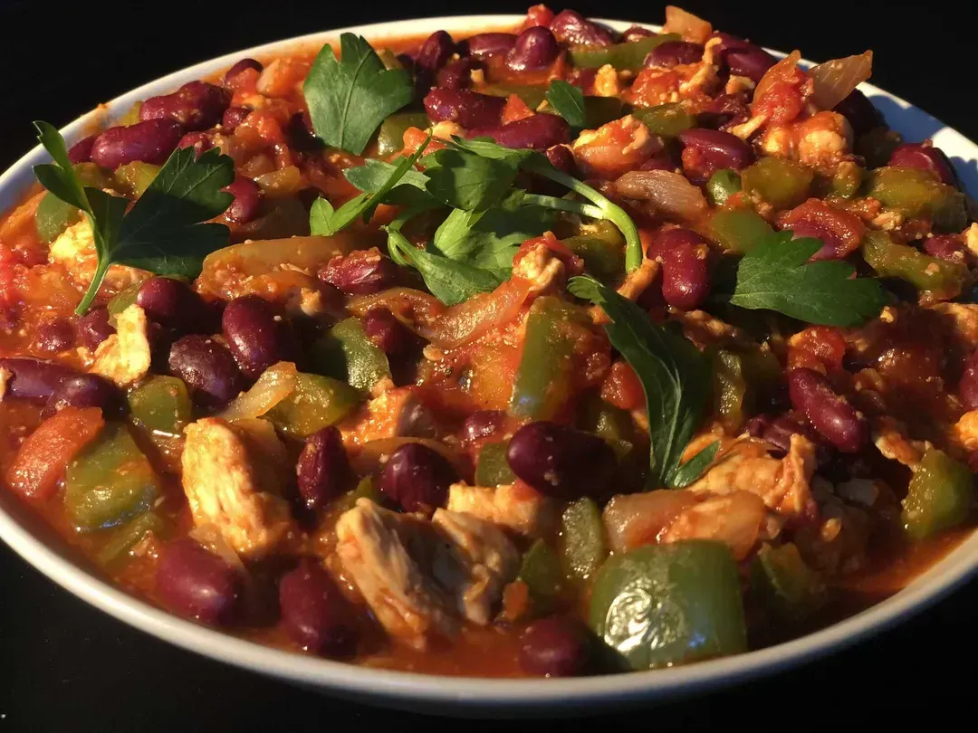 In a shallow dish, there are generous chunks of chicken, kidney beans, and bell pepper bathed in chili and tomato sauce.