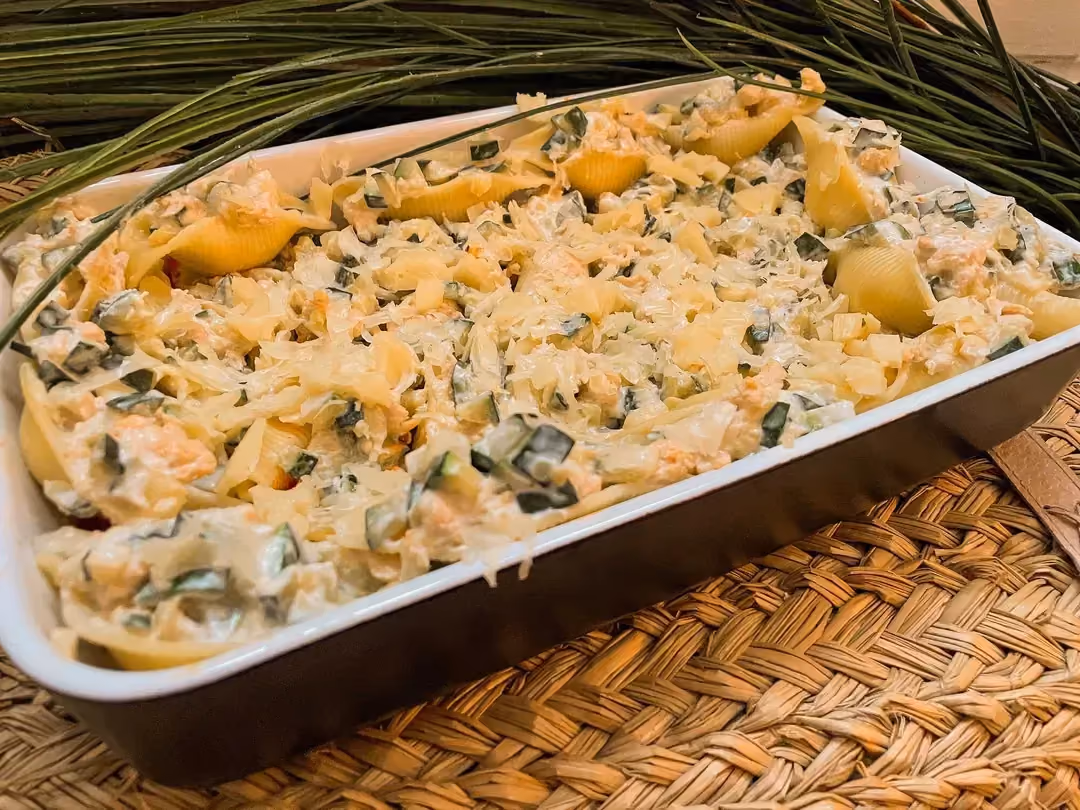 Conchiglioni stuffed with zucchini, St-Môret, and chicken are presented in a black baking dish, with a plant in the background.
