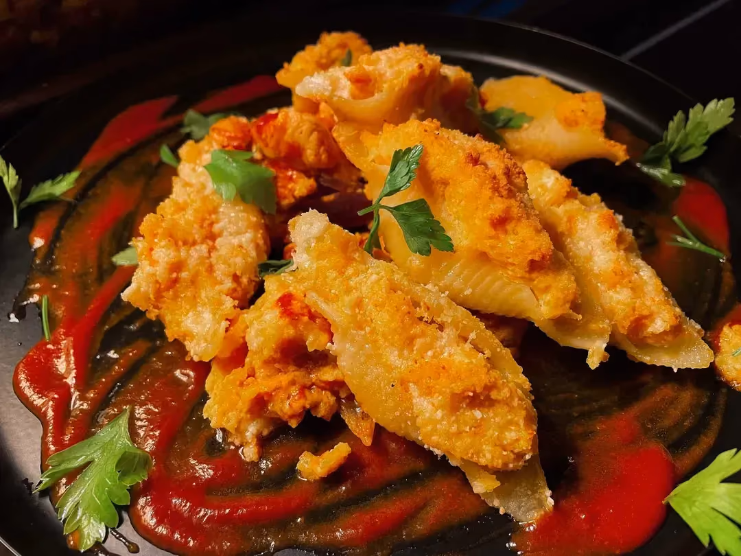On a bed of tomato sauce are the stuffed conchiglioni. A few parsley leaves are placed on top.