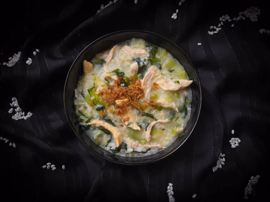Le congee au poulet composé de riz blanc, de chou pak-choï, de ciboulette coupée finement et de poulet effiloché est présenté dans un plat creux.