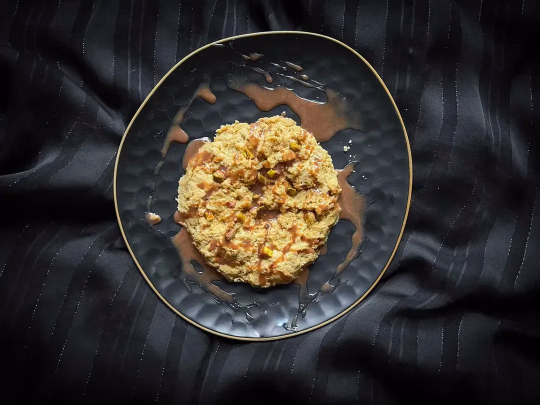 The maxi pistachio protein cookie with its chocolate sauce is presented in a blue honeycomb-patterned bowl.