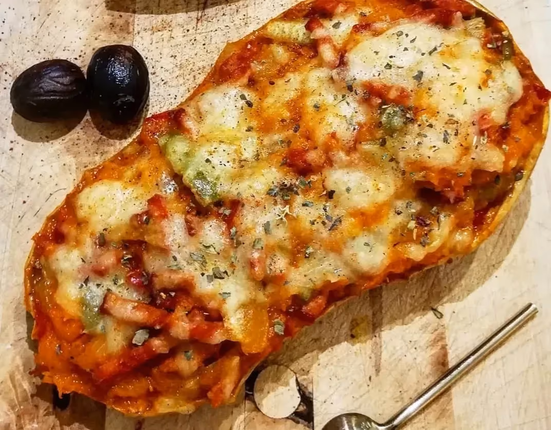 The squash’s thick skin serves as a vessel for the filling. The melted cheese completes the recipe. Two black olives sit beside it.