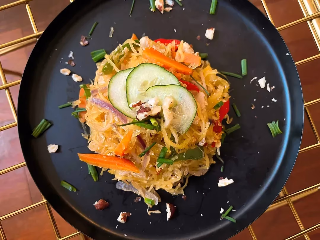 Cette recette de courge spaghetti façon Pad Thaï est présenté sur une poêle peu profonde. Les ingrédients forment une pyramide au centre de la poêle.