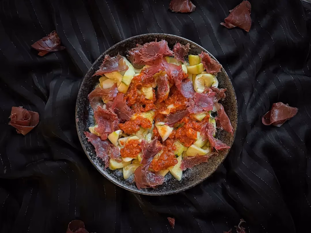 The indulgent recipe for zucchini with truffle tomato sauce and dried meat is presented on a blue plate.