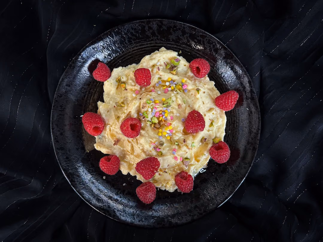On a black plate is vanilla cream topped with crushed pistachios and maple syrup.