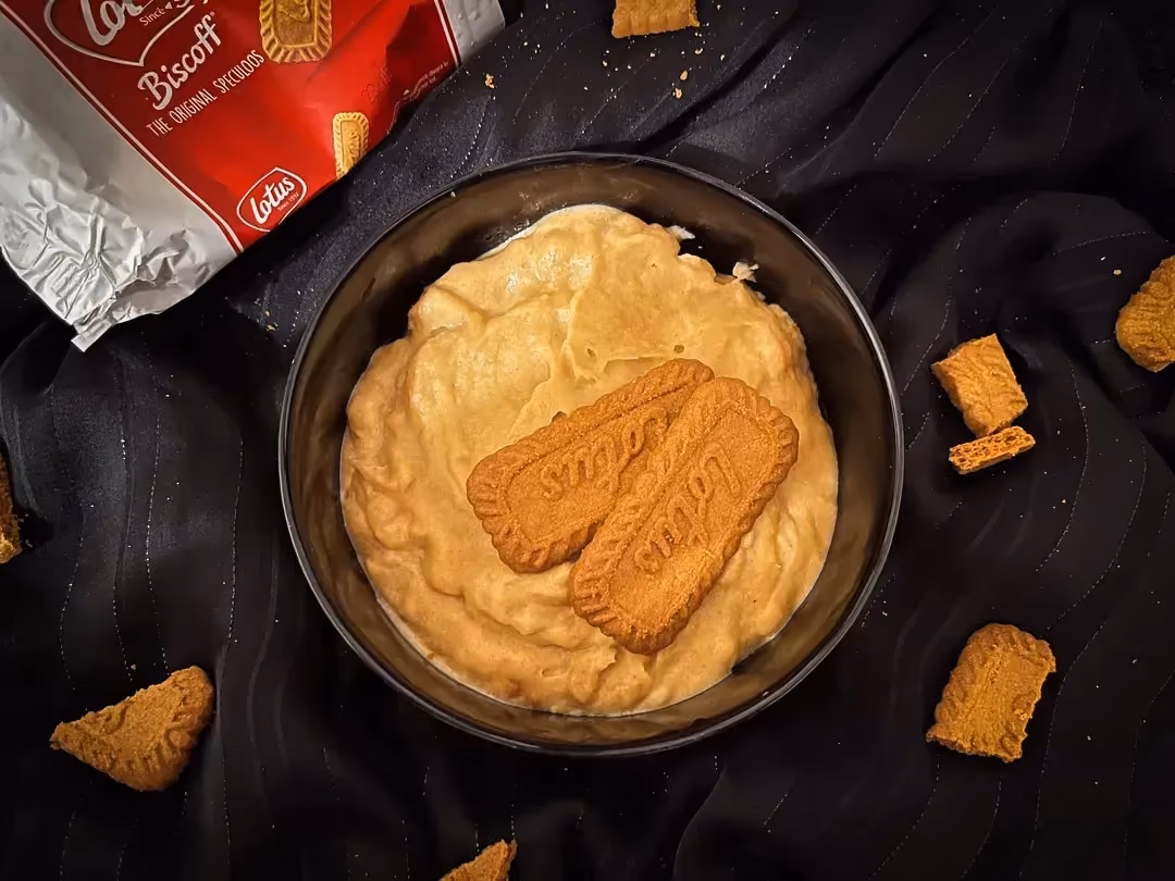 On a countertop sits a small bowl containing speculoos cream made with crushed speculoos cookies. Two whole speculoos cookies are above it.