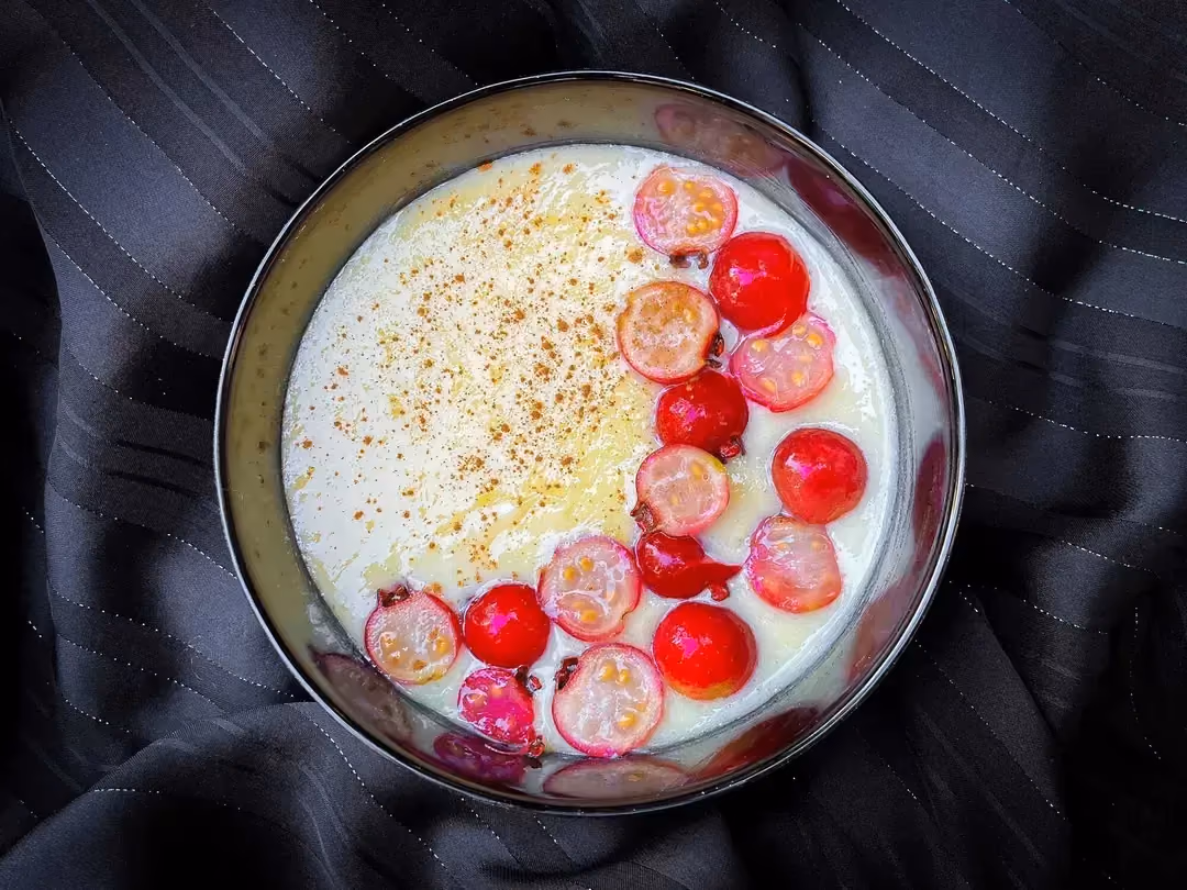 The protein cream of rice is in a small bowl. The topping is made of red berries, some whole and others cut in half.