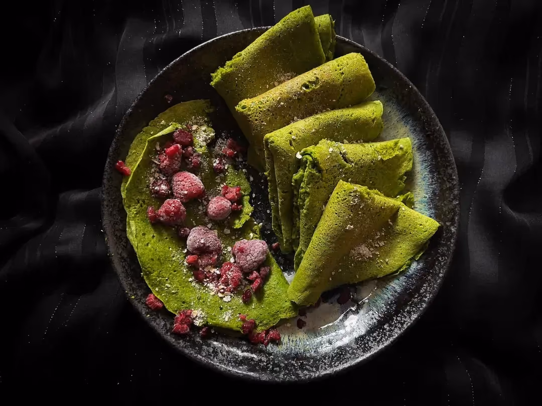 Huit crêpes au vert intense grâce aux épinards sont présentées dans un petit saladier de couleur bleu.