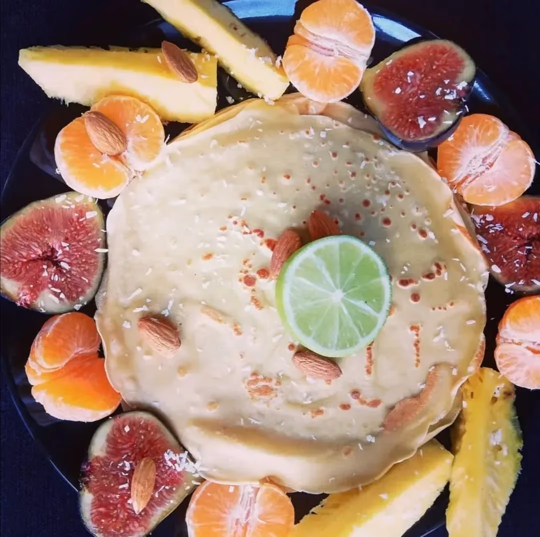 Sur la pile de crêpes, il y a des amandes et un demi citron vert. Autour sont disposées quelques demi figues et des mandarines ouvertes en deux..