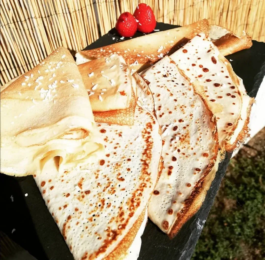Beautiful golden-brown crêpes are folded in half or into quarters and placed on a black plate.