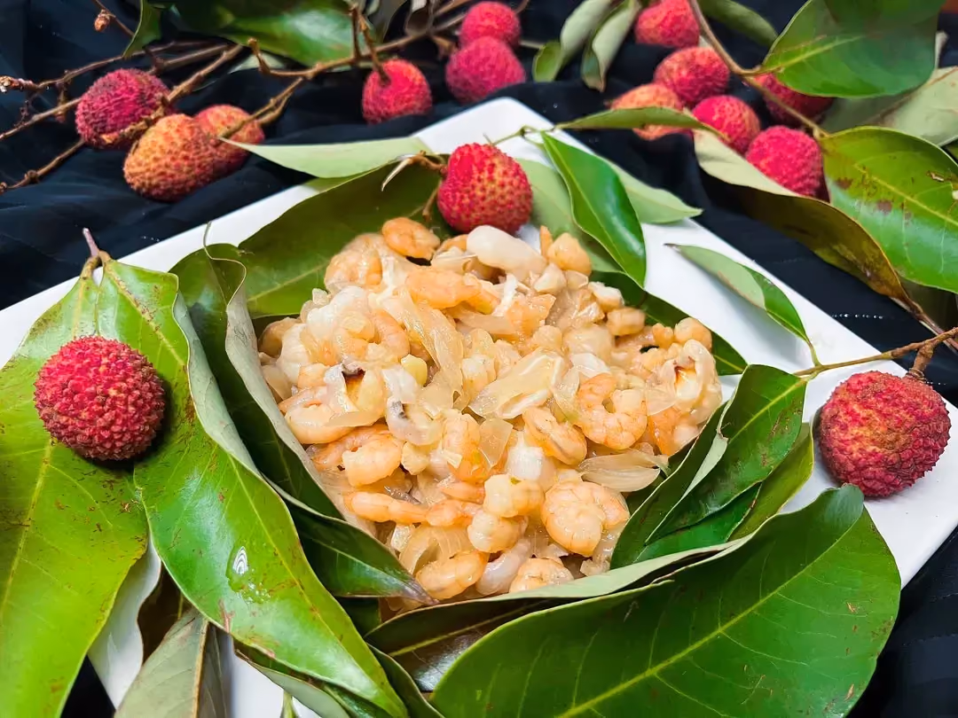 On a bed of lychee leaves are peeled shrimp with lychees cut in half. The whole dish is served with a little soy sauce.