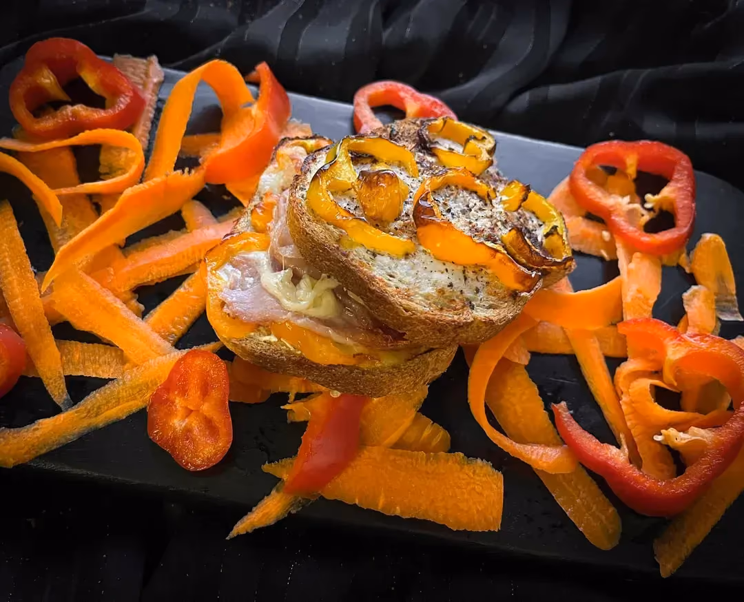 The recipe for croque-monsieur with Comté, Serrano ham, and peppers is presented on a black cutting board.