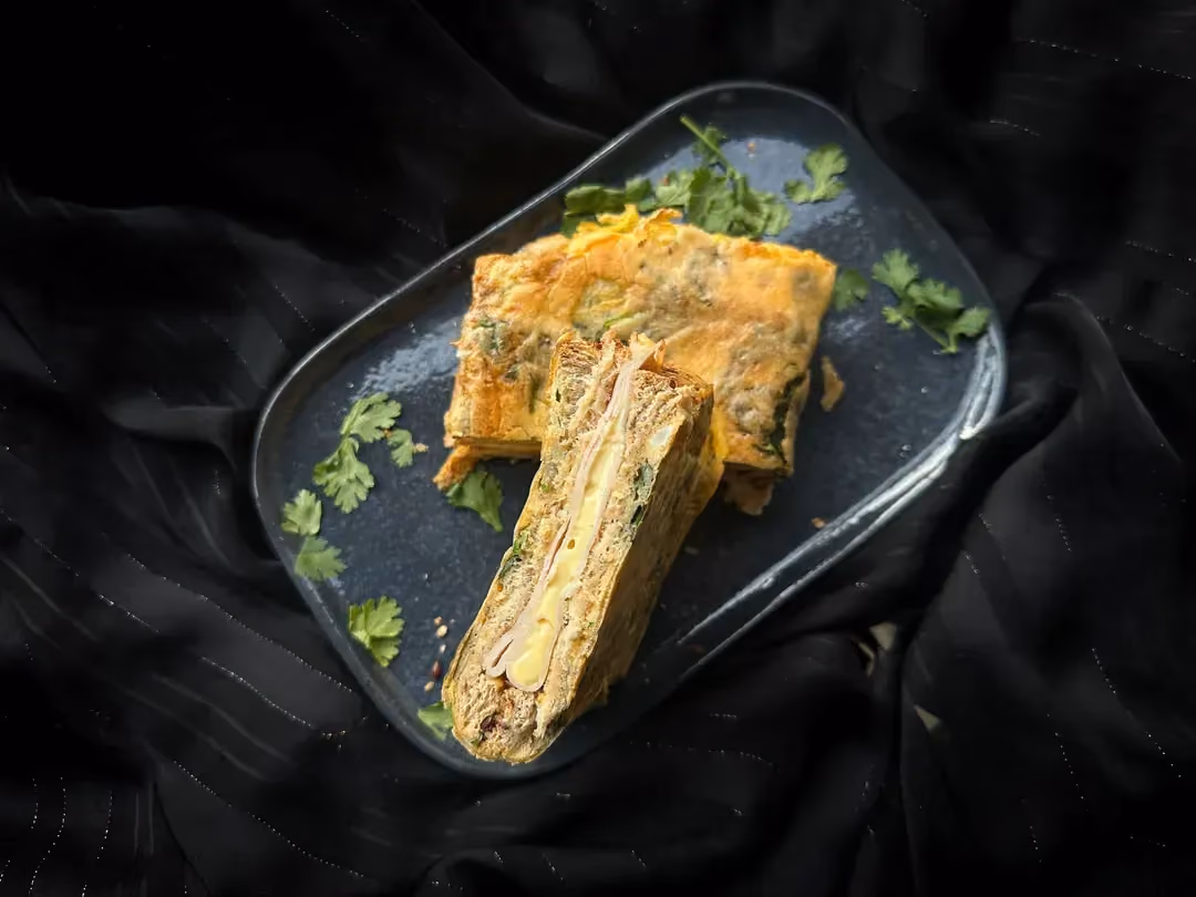 Trois grosses parts de croque omelette sont déposées sur un plat rectangulaire peu profond de couleur bleu.