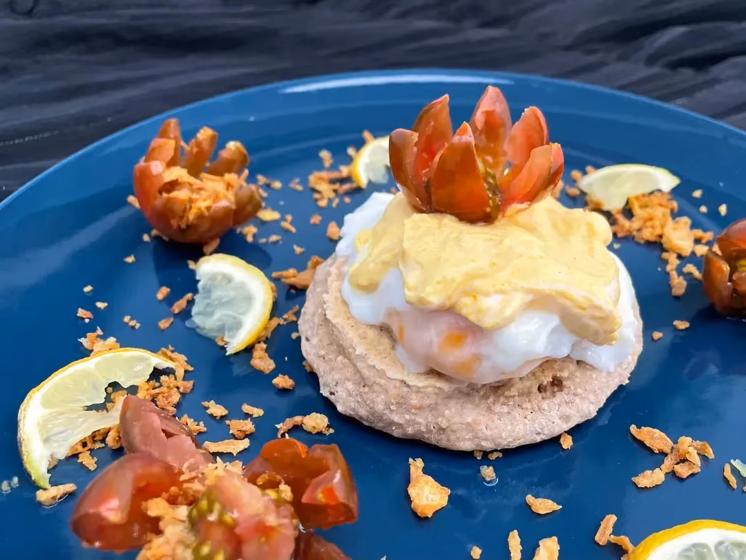 Le crumpet est surmonté par les oeufs et recouvert de la sauce à base de fromage blanc. Le tout est présenté sur une belle assiette de couleur bleue.