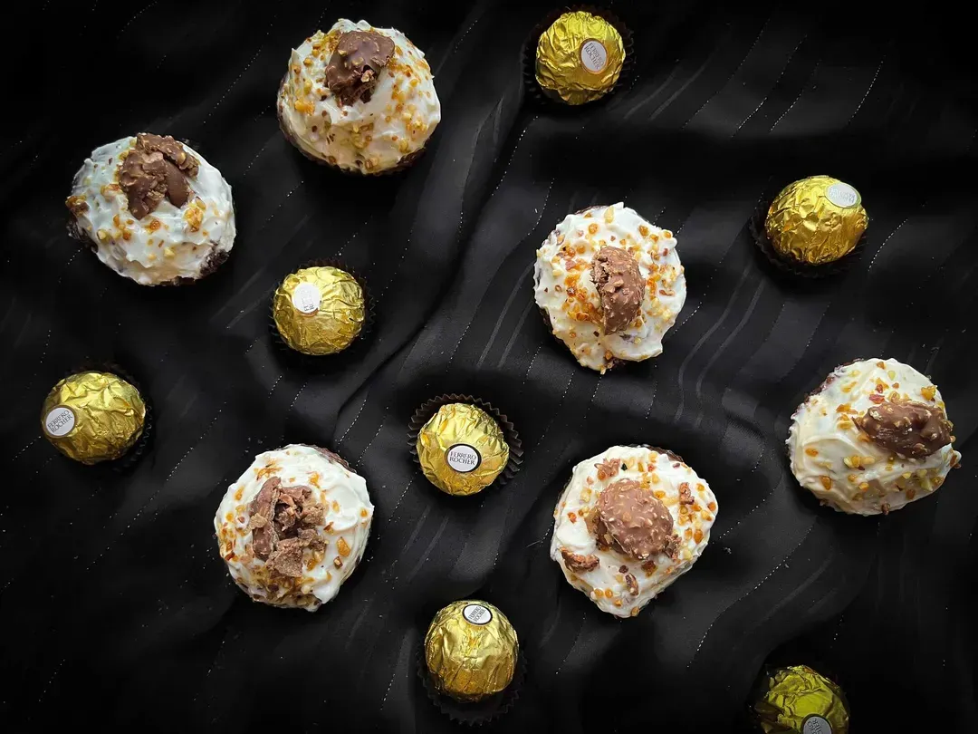 Six small cupcakes are accompanied by seven Ferrero Rocher.